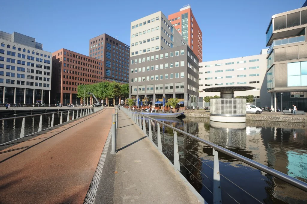 Fiets- en wandelpad langs het water bij het Johanna Westerdijkplein in Den Haag, omringd door moderne kantoorgebouwen.